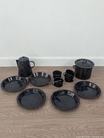 Entire 12-piece enamelware set laid out: coffee pot, stock pot with lid, four mugs, four plates, two bowls