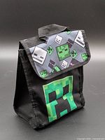 Front angled view displaying creeper face graphic, Velcro flap, carry handle