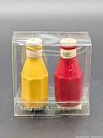 Front view of boxed Tag ketchup & mustard shakers