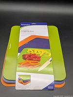 Front view of packaged set showing green, orange, purple mats and knife/vegetable image