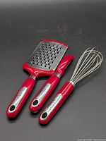 Three red-handle KitchenAid tools displayed on black background