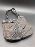 Front view of dark brown leather handbag with black handles and center ruched seam