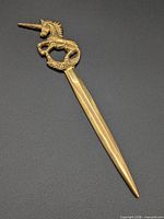 Full view of brass unicorn letter opener on black background