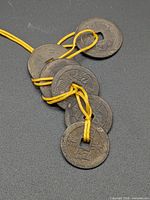 Six Chinese Feng Shui coins on yellow cord displayed on black background
