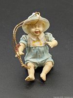 Front view of bisque baby ornament showing clothing, facial details and gold cord