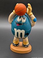 Front view of blue M&M basketball player dispenser on base