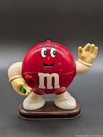 front view of red M&M candy dispenser on base, waving