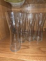 Group of clear glass pilsner beer glasses inside cabinet