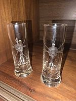 Two cylindrical etched crystal flutes without visible handles on wooden shelf