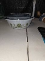 Side view of a white milk glass Glasbake casserole with green clover vine decoration and clear lid