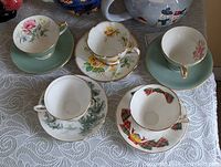 Five teacups with corresponding saucers displayed on lace cloth