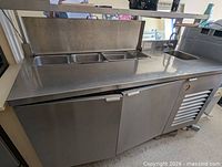 Full view of stainless prep fridge showing lid, pans, sink, and doors
