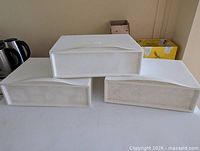 Three white plastic wall-mount drawers stacked