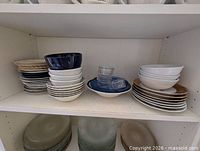 Shelved dinnerware showing left stack of mixed pattern plates, middle stack of white bowls under navy bowl, right stack with ramekins and brown-rim plates