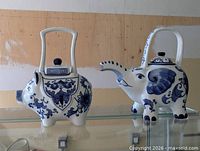 Front view of both animal-shaped teapots on glass shelf
