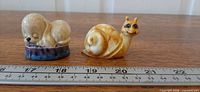 Snail and puppy figurines side by side with ruler showing scale