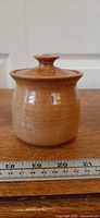 Front view of glazed stoneware jar with lid, ruler showing scale