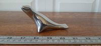Left side view of polished aluminum seal figurine beside ruler showing length ~6 in.