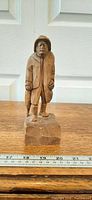 Full front view of carved wood figure on base with ruler for scale