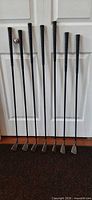 Seven Ben Hogan irons standing against door