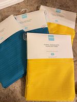 Front view of three packaged tablecloths showing yellow and teal colors