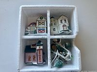 Styrofoam tray showing three ceramic buildings, four trees, lights and figurines