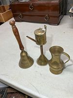 Three brass items: hand bell, oil lamp, jug on tabletop