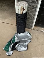 Rolled camp mat in black carry wrap with folded silver-green ground sheet in front