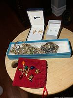 Group shot of all jewelry pieces on table including boxed items, blue tray of assorted pieces and red pouch