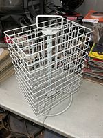 Overall view of white wire rotating display rack showing handle, grid sides and round base