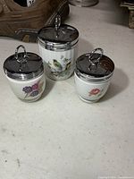Three egg coddlers grouped together showing sizes and motifs