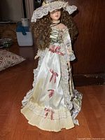 Front view of porcelain doll standing, showing full gown and hat