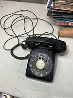 Full view of black rotary phone with handset, cords and rotary dial