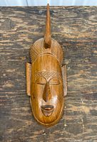 Front view of wooden wall mask showing carved facial features and crest
