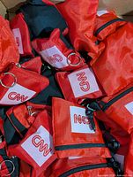 Box of red CNN-logo foldable nylon pouches showing key rings, clips and zipper detail