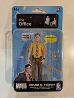 Front view of sealed Dwight K. Schrute action figure on card showing figure and accessories