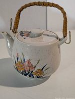 Toyo ceramic teapot showing floral decal, rattan handle attached, lid in place