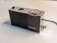 Front angled view showing speaker grille, tuning dial, wrist strap