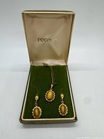 Open Peoples box showing pendant necklace and two earrings on green velvet