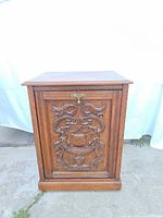 Front view of carved oak cabinet showing brass latch and plinth base