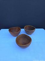 Three teak bowls upright on blue surface showing shape and grain