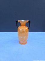 Front view of orange lusterware vase with two black handles and scalloped rim
