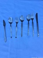 Seven stainless steel flatware pieces laid out side-by-side