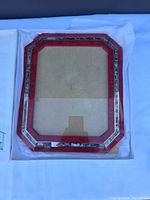 Front view of red lacquer picture frame showing mother-of-pearl inlay and glass