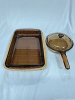 Rectangular amber glass baking dish nested in wicker basket beside round amber glass skillet with lid