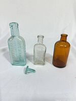 Front view of three antique glass bottles showing colors and one loose stopper