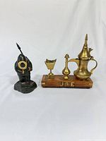 Front view of stone Inuit figure beside brass pieces on wood base