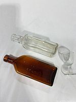 Amber bottle, clear bottle, and cordial glass laid flat