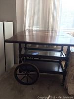 Side view of vintage wooden tea cart with raised drop leaf extensions and visible wear on top surface