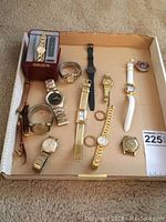Full assortment of 11 wristwatches displayed in cardboard tray with some watches stacked and removable bezels shown separately. Watches include various brands and styles in gold, silver-tone, black, and white bands.